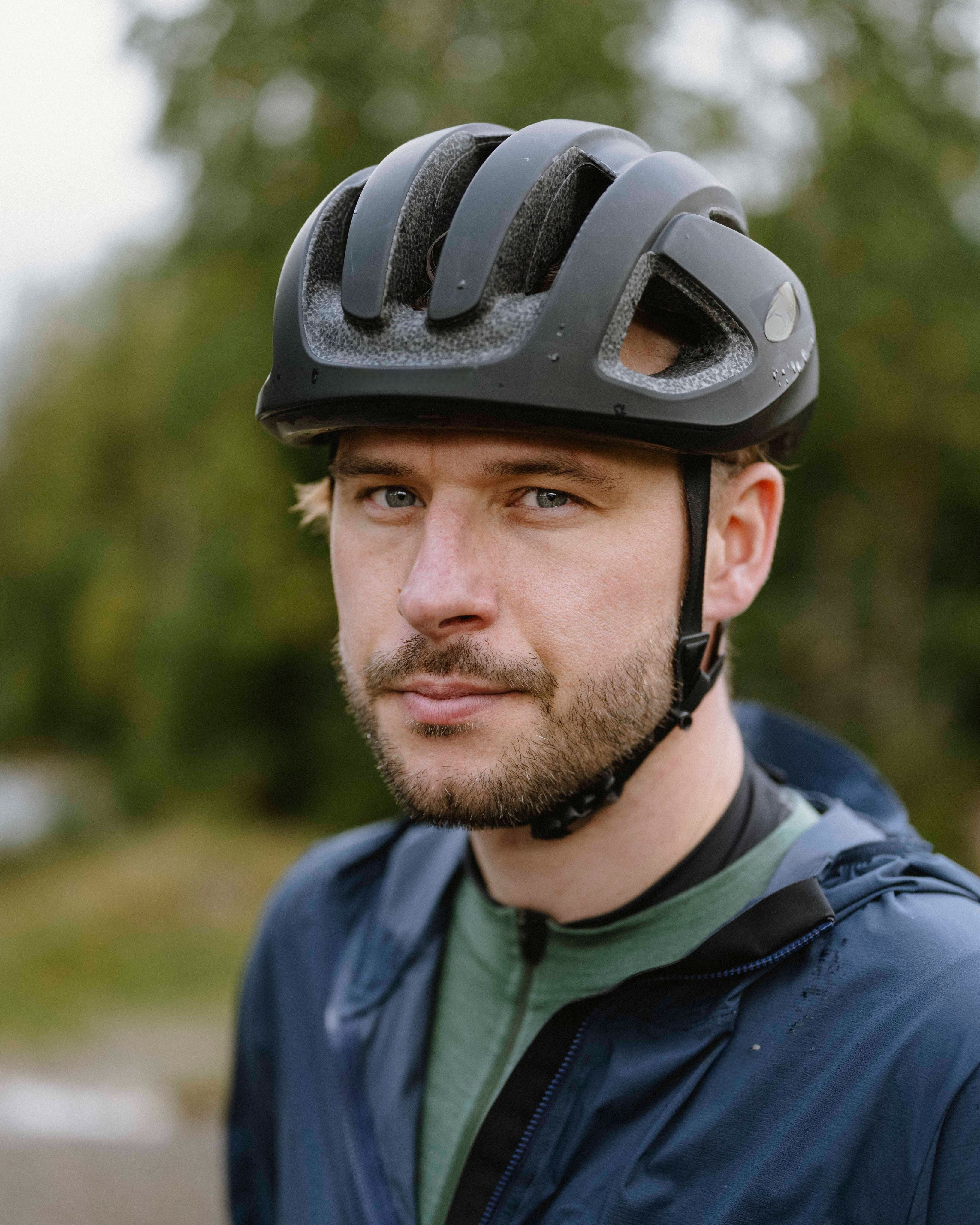 Man wearing a black helmet outdoors with blurred greenery in the background