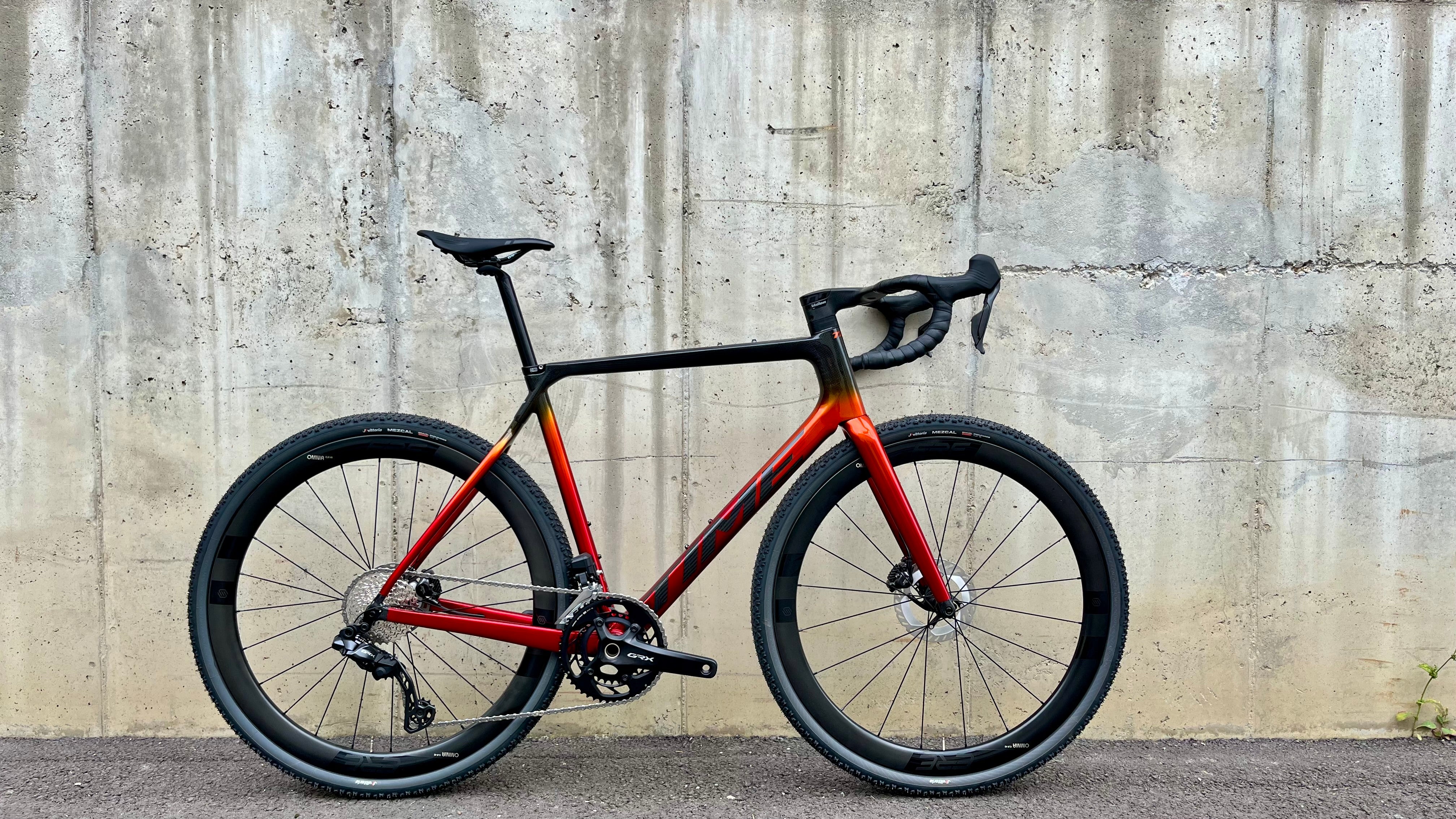 Red and black bicycle leaning against a concrete wall